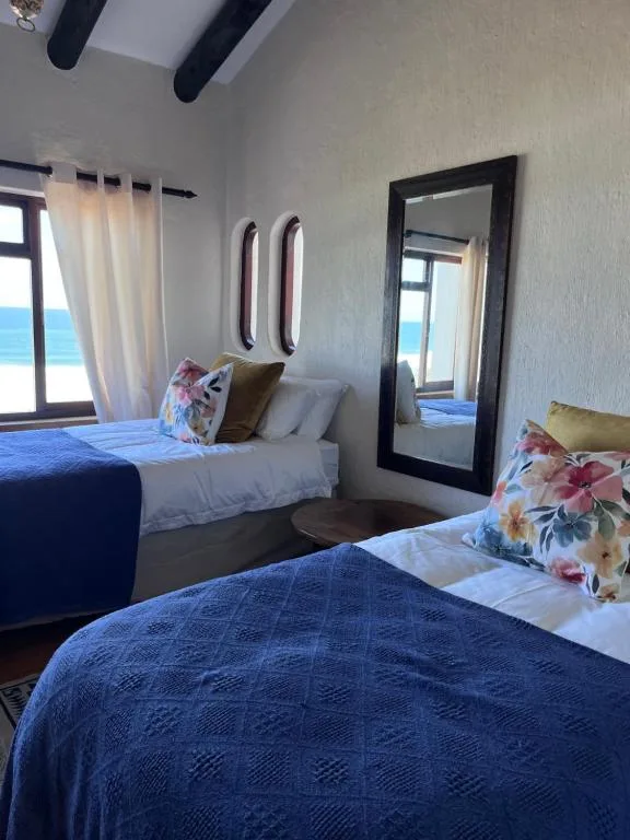 Bright coastal bedroom with two beds, ocean views, and black-framed mirror