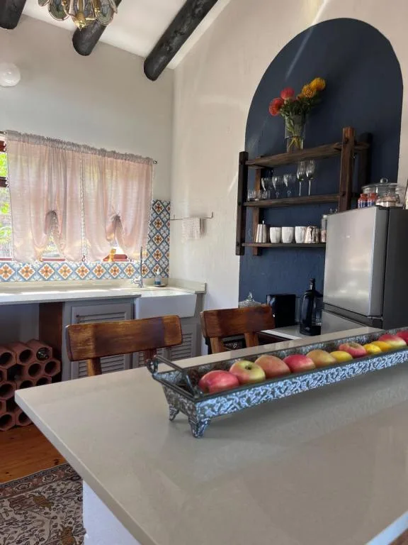 Open-plan kitchen with white counters, dark blue accent wall, wooden chairs, and fresh fruit display