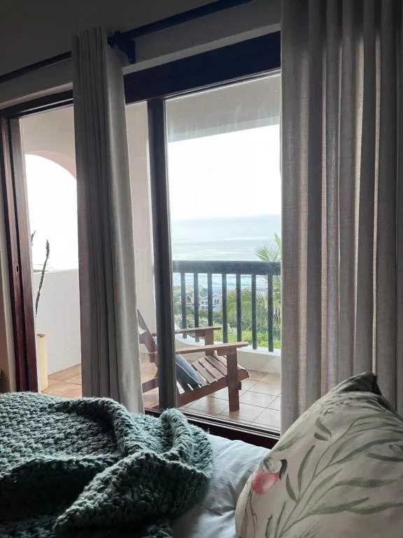 Ocean and coastal landscape visible through bedroom glass doors and deck railing