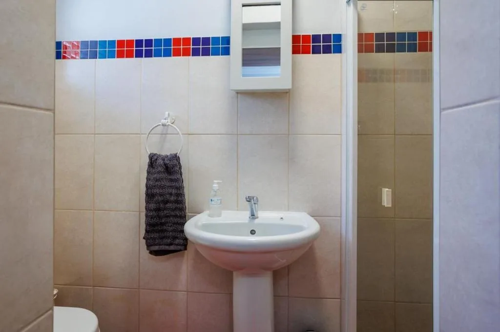 Bathroom with pedestal sink, colorful tile trim, and shower enclosure