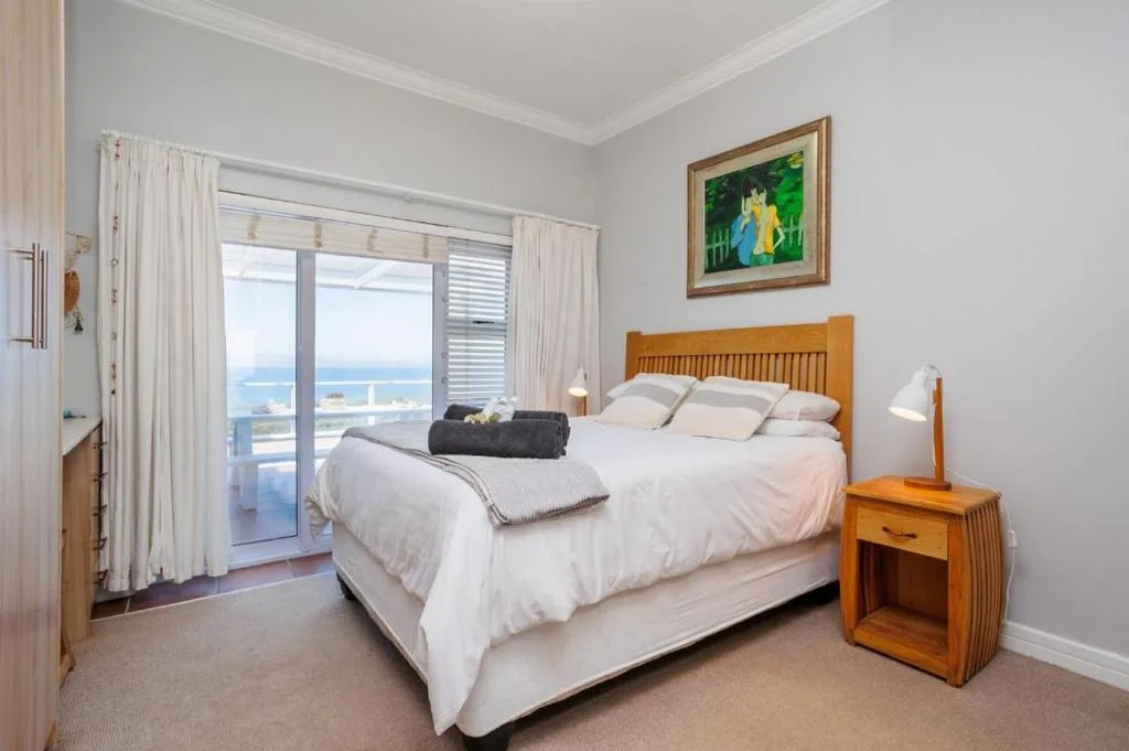 Spacious bedroom with ocean view, wooden headboard, white linens, and balcony access