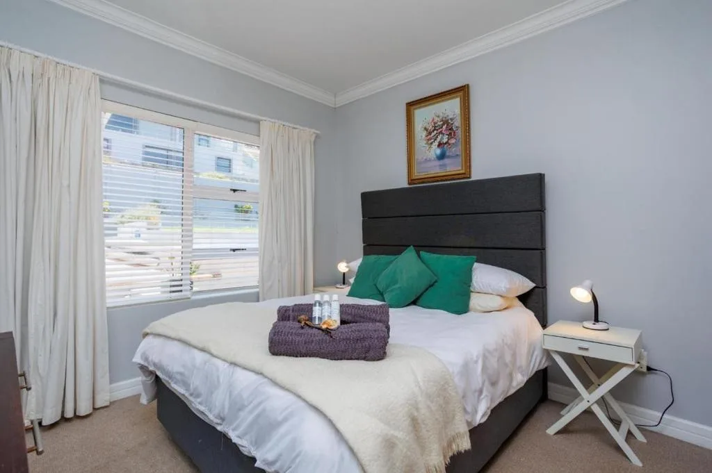 Bright bedroom with black headboard, green pillows, and large window