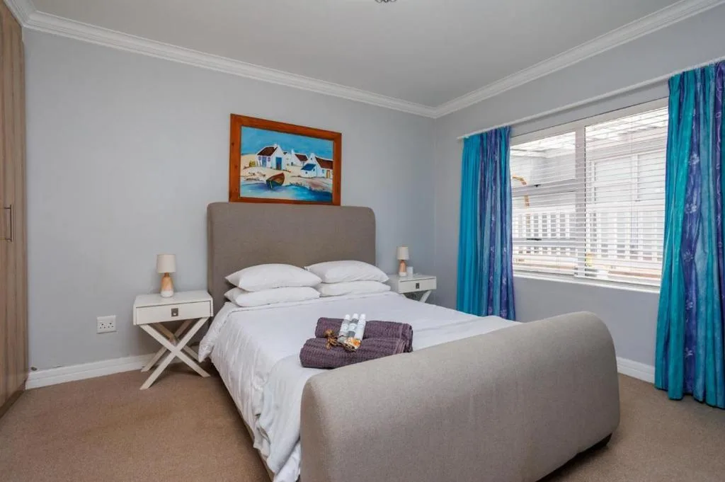 Bright bedroom with queen bed, grey upholstered headboard, turquoise curtains