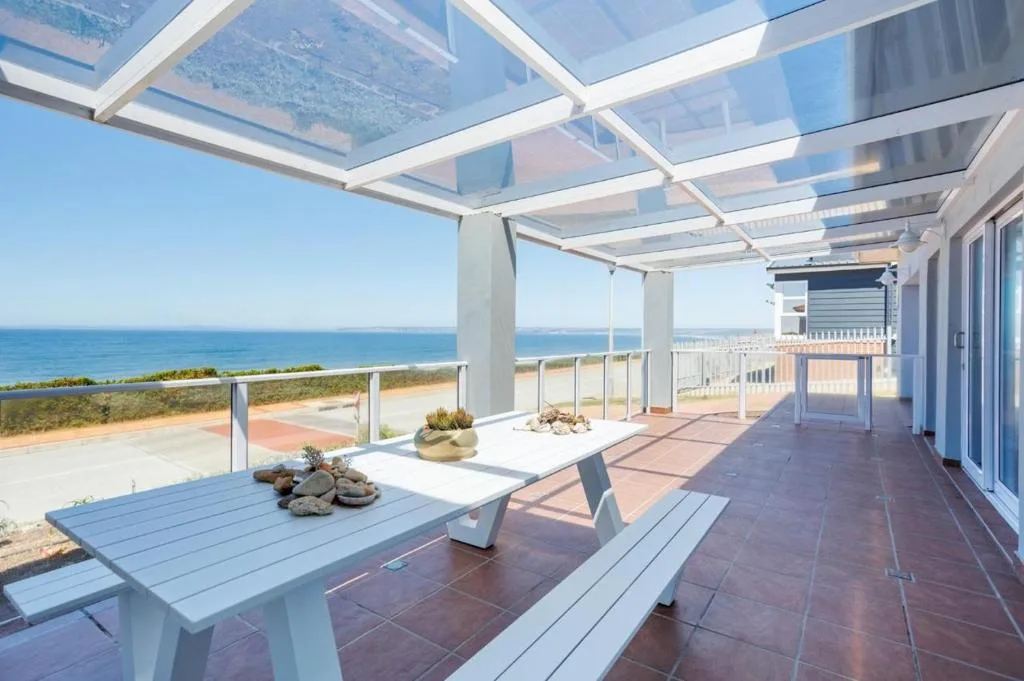 Ocean-view deck with glass pergola, dining table, and coastal horizon