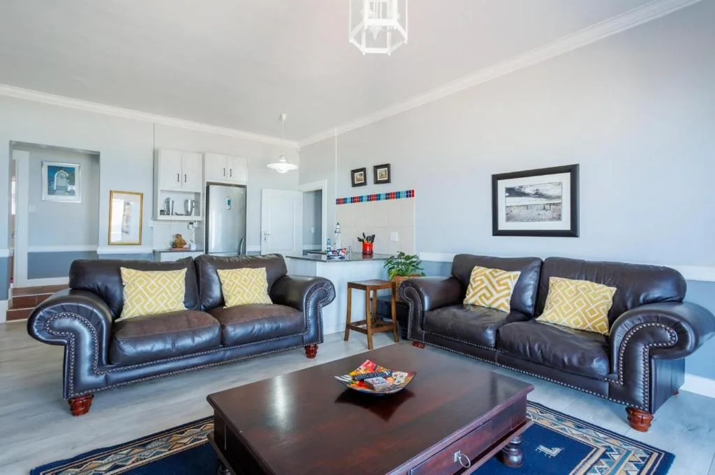 Spacious lounge with two dark leather sofas, yellow cushions, and wood coffee table