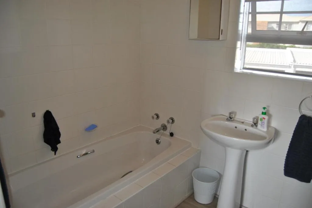 Clean bathroom with bathtub, pedestal sink, and window for natural light