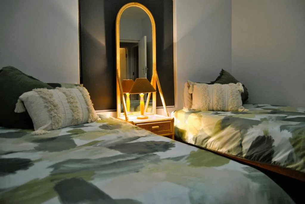 Modern bedroom with twin beds, decorative pillows, and illuminated gold mirror