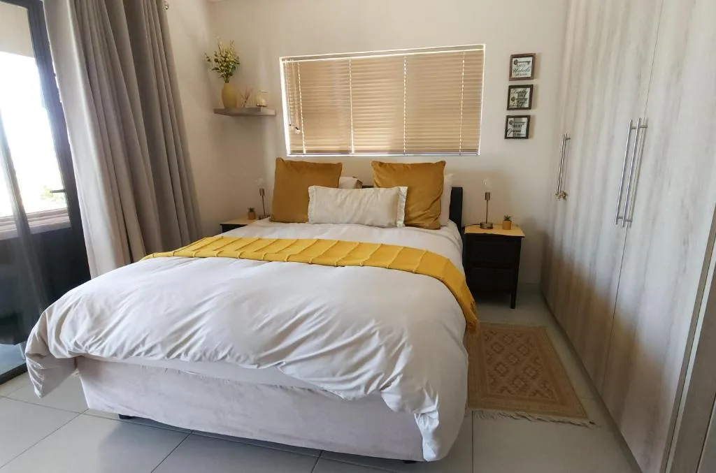 Bright bedroom with queen bed, mustard yellow accents, and natural light from windows