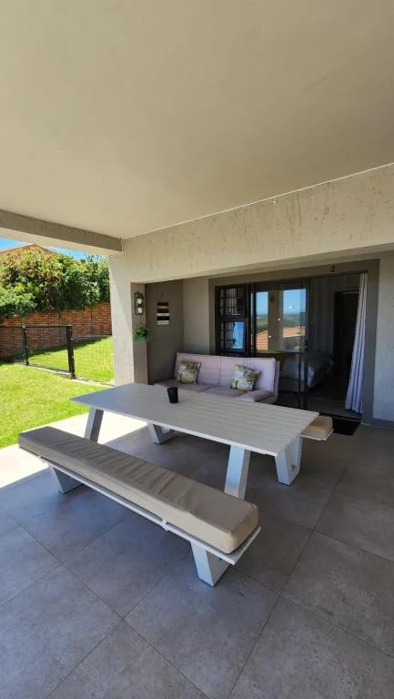 Covered outdoor patio with dining table and green lawn beyond