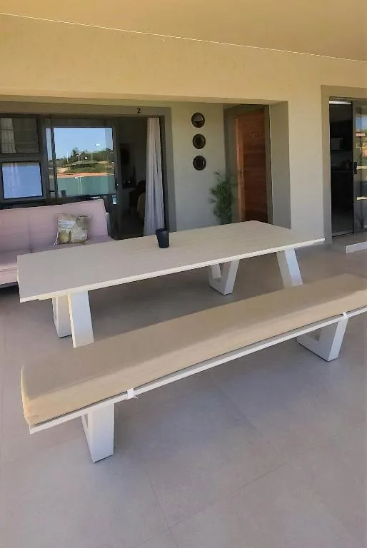 Modern outdoor deck with white benches and dining tables, garden views