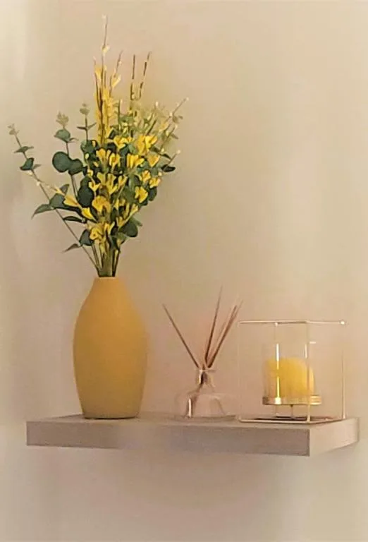 Yellow vase with flowers and decorative candles on shelf