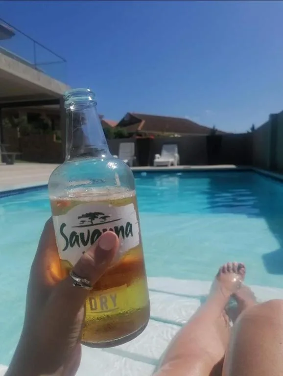 Beer bottle held poolside with sparkling blue swimming pool in background