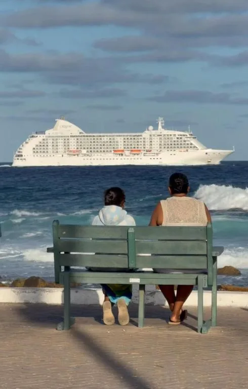 Couple on beach bench gazing at ocean with cruise ship on horizon
