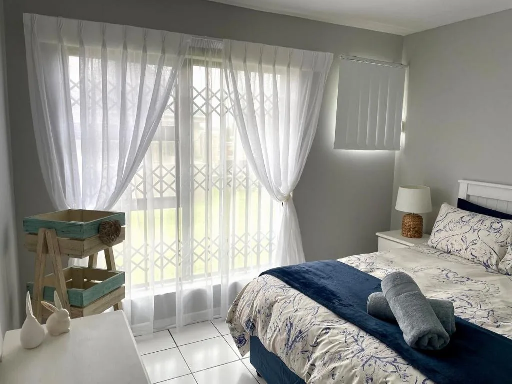 Bright bedroom with patterned bedding, sheer curtains, and garden views
