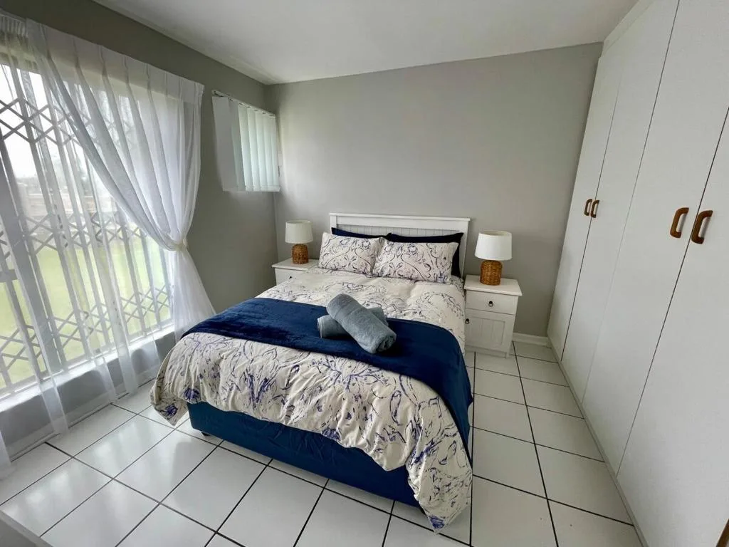 Bright bedroom with queen bed, white wardrobes, and garden view windows