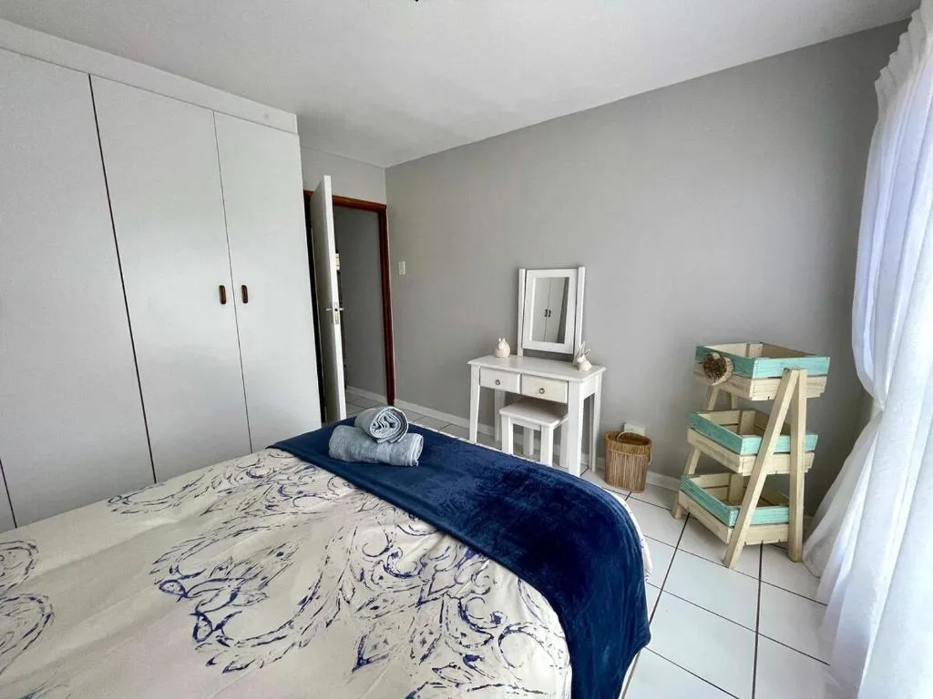 Bright bedroom with queen bed, white wardrobe, vanity mirror, and coastal decor