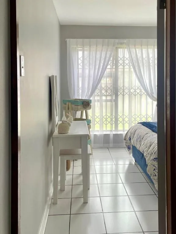 Bright bedroom with blue bedding, white furniture, and sheer curtains framing garden views
