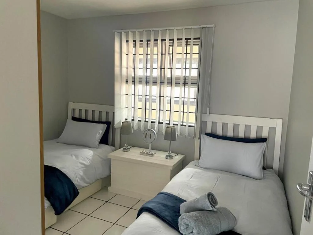 Twin bedroom with white bedding, bedside table, and vertical blinds over window