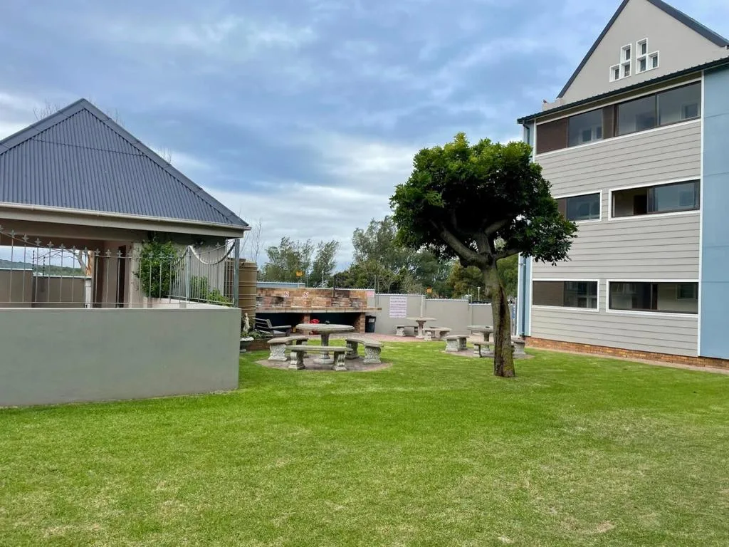Modern multi-story accommodation building with manicured lawn and outdoor fire pit area