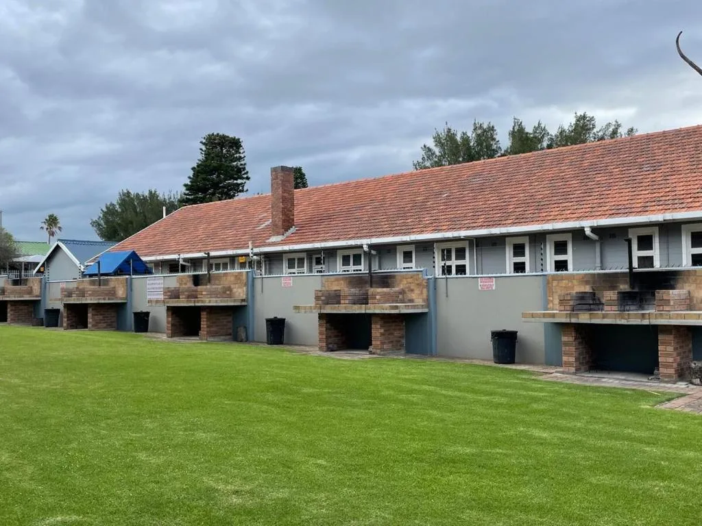 Modern beige building with terracotta roof and brick braai areas on green lawn