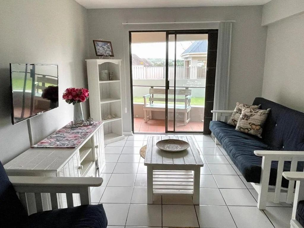 Bright lounge with blue sofa, TV, white storage, opening to deck