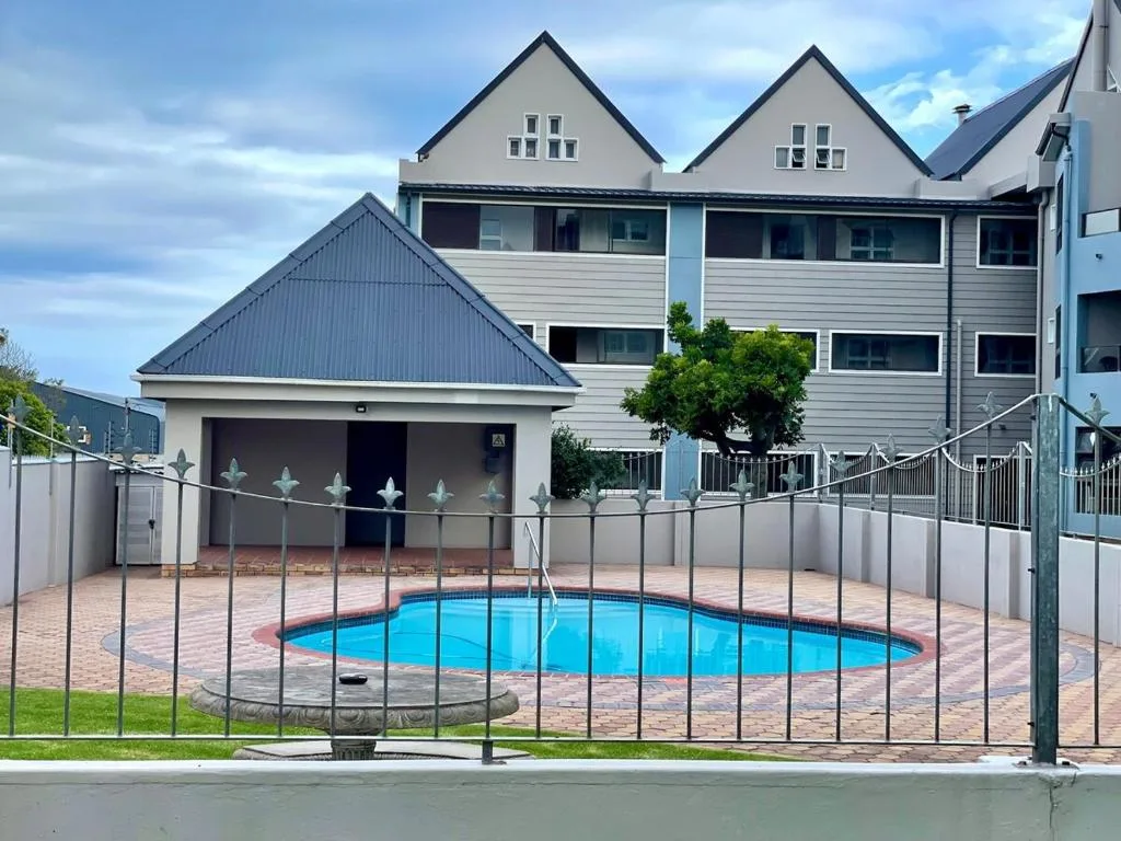 Bright blue swimming pool with safety fence and modern house backdrop