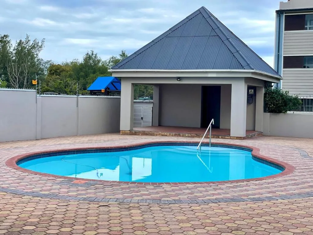 Bright blue oval swimming pool with brick paving and poolhouse behind