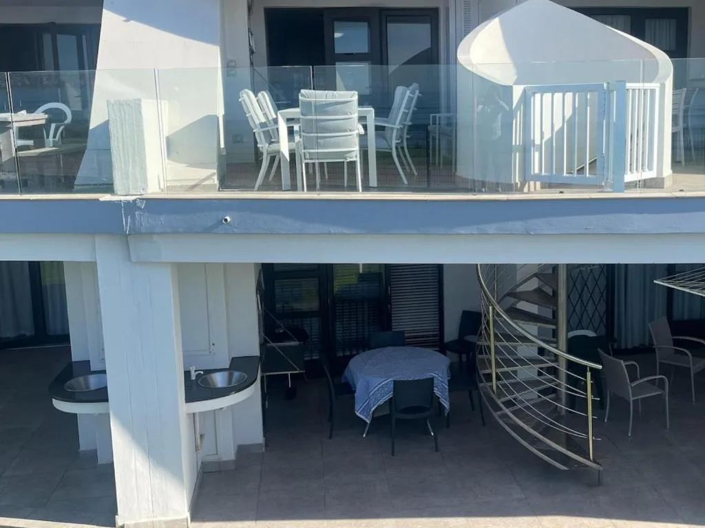 Multi-level waterfront deck with dining table, lounge chairs, and sea views