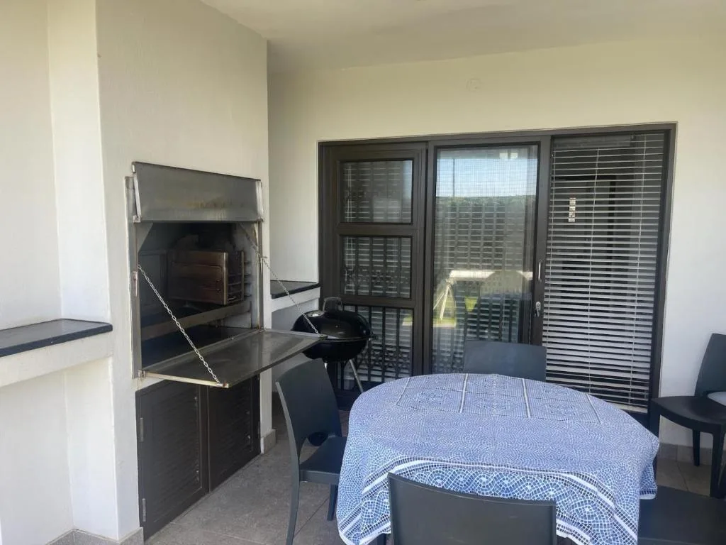 Covered outdoor patio with braai, dining table, and garden views