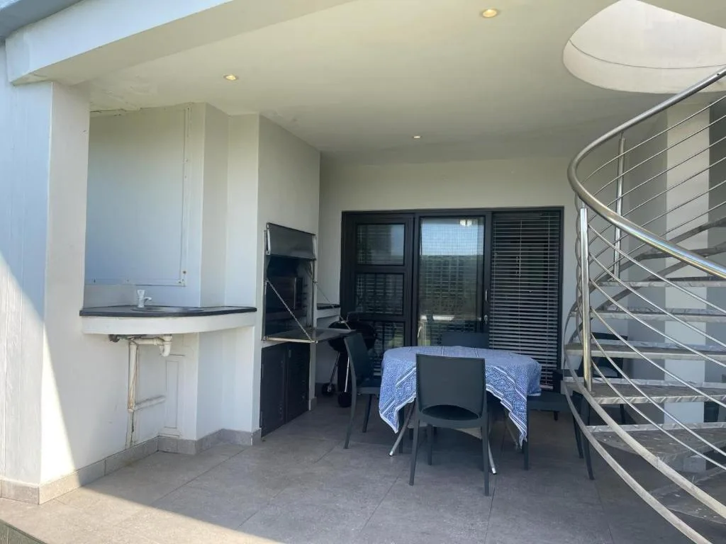 Covered outdoor deck with dining table, kitchenette, and metal railing stairs
