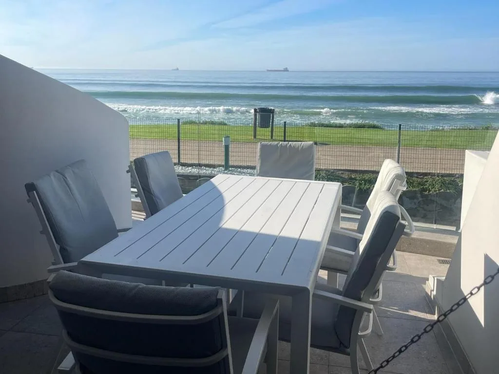 Outdoor dining area overlooking beach with ocean waves and grassy dunes
