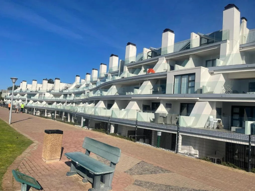 Modern white apartment building with multiple units and pitched roofs along beachfront promenade