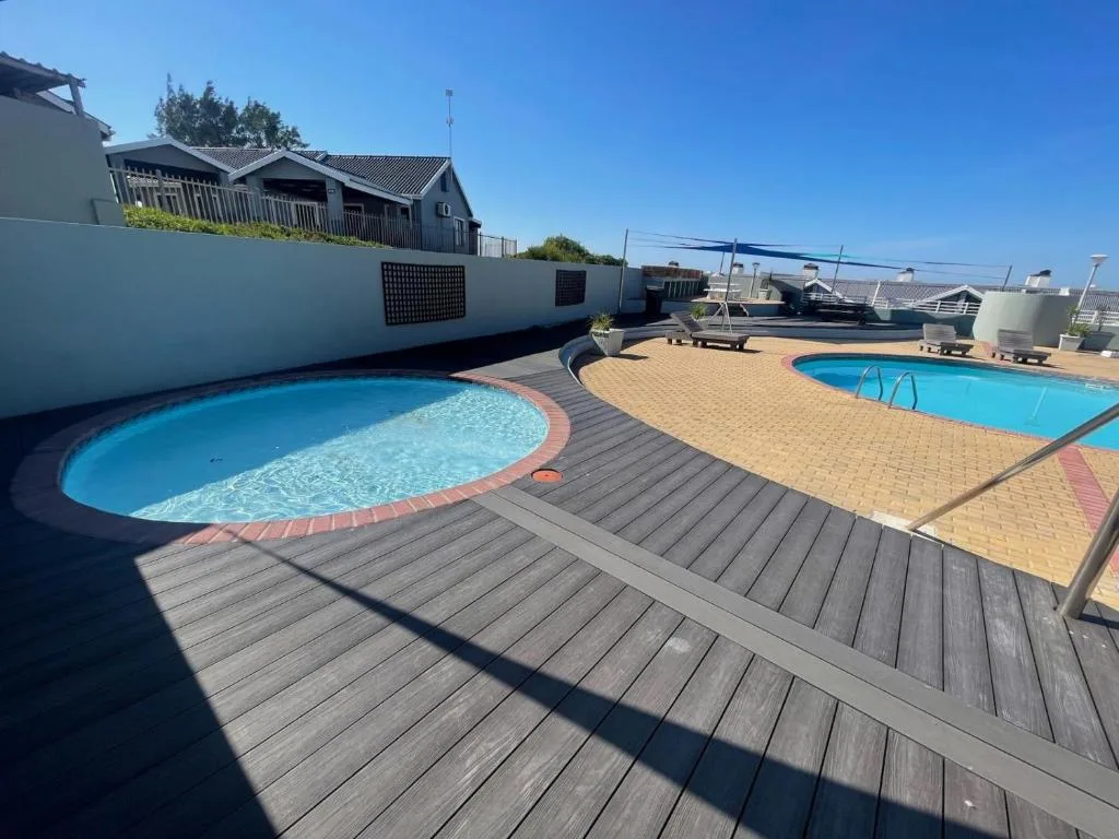 Two swimming pools with wooden deck and accommodation building in background