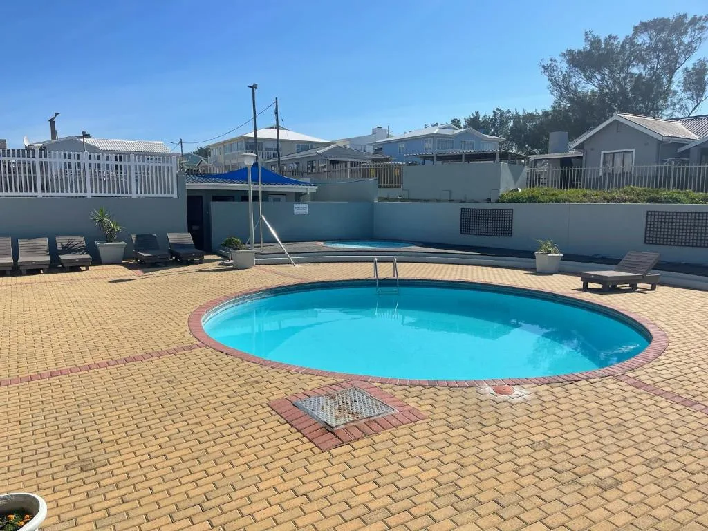 Bright blue oval swimming pool on brick patio with loungers and coastal homes