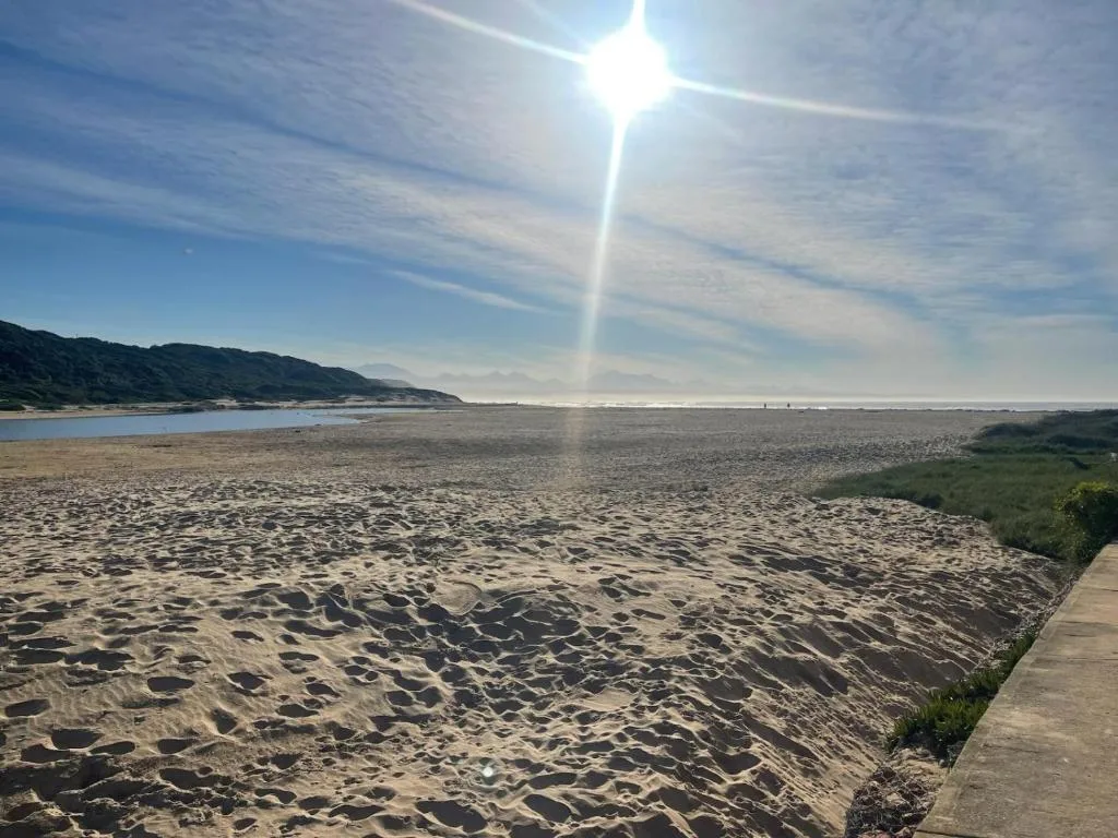 Sandy beach with ocean, mountains, and bright sunny sky view