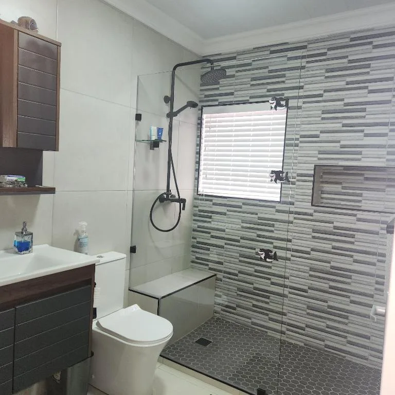 Modern bathroom with walk-in shower, grey tile walls, vanity, and toilet