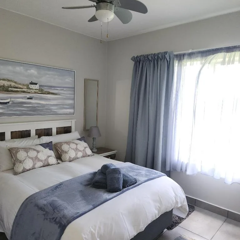 Bright bedroom with white bed, patterned pillows, coastal artwork, ceiling fan