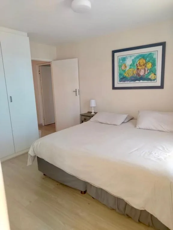 Bright bedroom with queen bed, white bedding, and framed coastal artwork