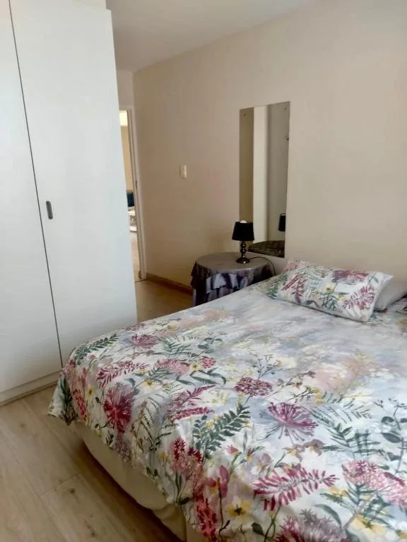 Bedroom with floral bedding, mirror, and bedside lamp