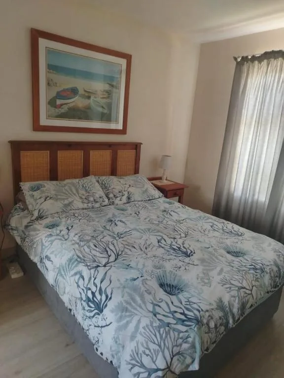 Bedroom with wooden bed frame, coastal-themed bedding, and framed ocean artwork