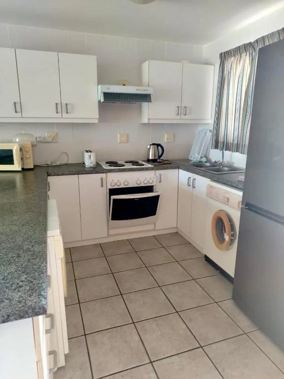 Modern white kitchen with stove, washing machine, and granite countertops