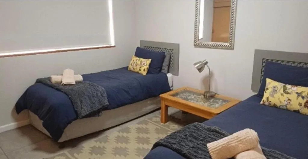 Twin bedroom with navy bedding, yellow accent pillows, and wooden side table