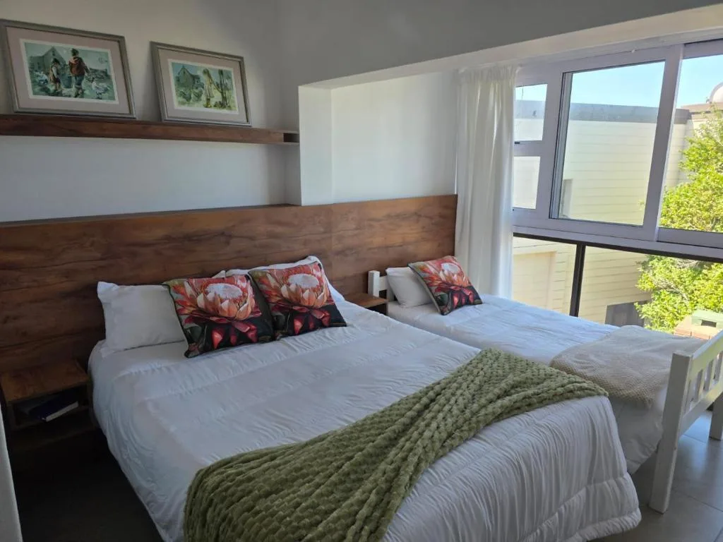 Bright bedroom with wooden headboard, white bedding, and garden views through large windows