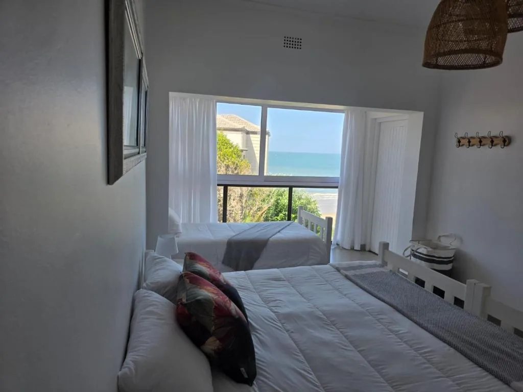 Bright bedroom with ocean view through large windows and coastal landscape