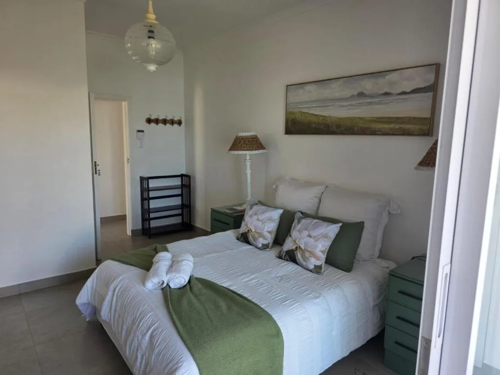Bright bedroom with queen bed, green accents, and coastal landscape artwork