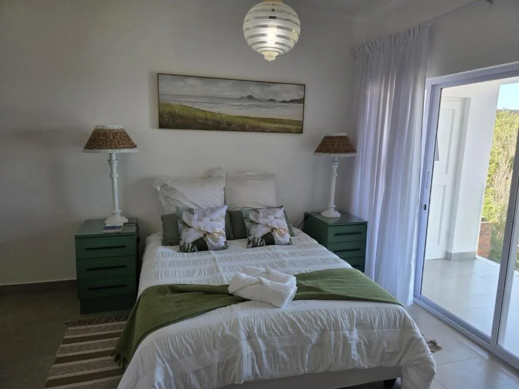 Bright bedroom with queen bed, green nightstands, and garden view through sliding doors