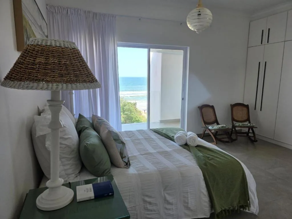 Spacious bedroom with ocean view through glass doors and coastal decor