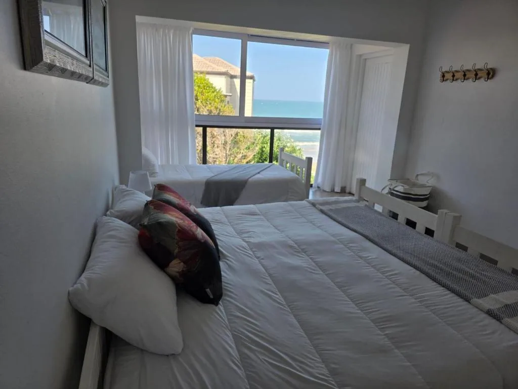 Bright bedroom with ocean view through large windows and coastal landscape beyond