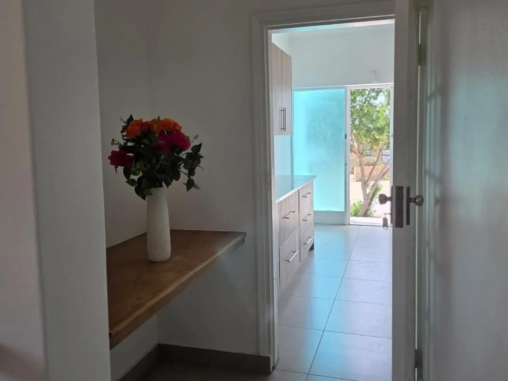 White vase with red roses on wooden shelf near entrance