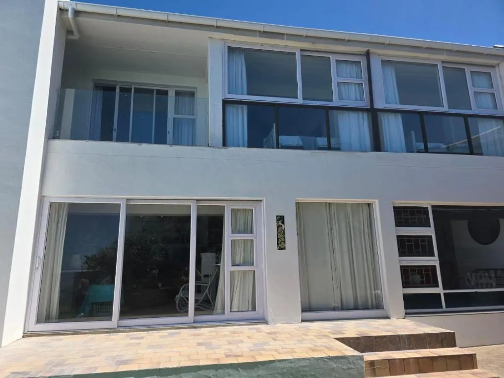 Modern white villa with large glass doors and upper-level balcony overlooking garden area